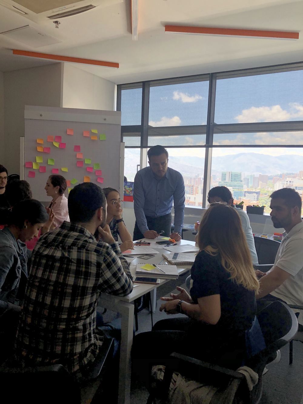 Participantes colaborando con notas adhesivas frente a los ventanales